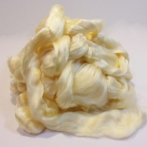 May include: A pile of pale yellow silk fibers, tightly bundled and arranged in a soft, flowing composition. The fibers have a subtle sheen, suggesting a delicate texture. The image showcases the natural color and texture of the raw silk material.