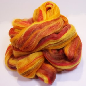 May include: A pile of colorful wool roving in shades of red, orange, and yellow. The wool is arranged in a loose, swirling pattern.