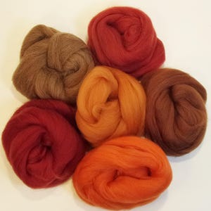 May include: Six balls of wool in various shades of red, orange, and brown. The wool is arranged in a circle on a white background.