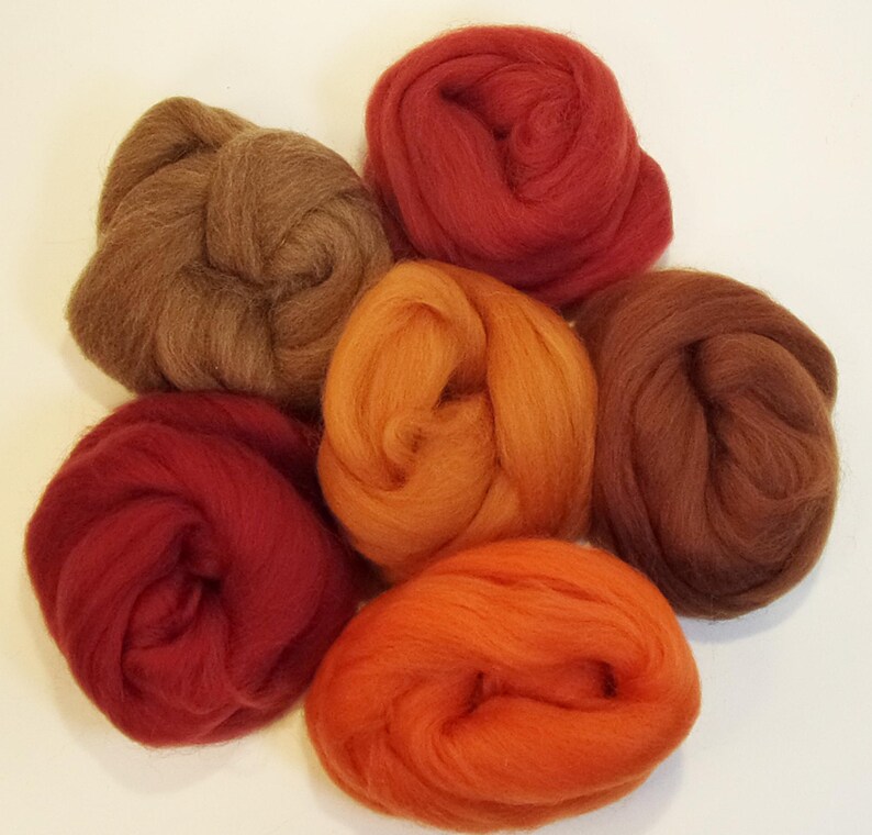 May include: Six balls of wool in various shades of red, orange, and brown. The wool is arranged in a circle on a white background.