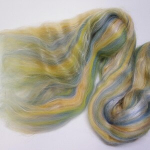 May include: A close-up of a pile of colorful fiber. The fiber is a blend of yellow, blue, and green hues, with a soft, flowing texture. The fibers are arranged in wavy patterns, creating a visually appealing display.