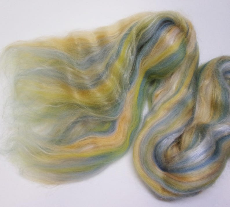 May include: A close-up of a pile of colorful fiber. The fiber is a blend of yellow, blue, and green hues, with a soft, flowing texture. The fibers are arranged in wavy patterns, creating a visually appealing display.