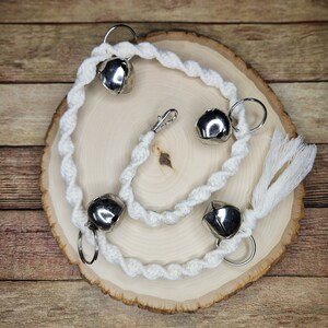 May include: White cotton rope with four silver bells attached. The rope is twisted and has a tassel at the end. The bells are attached to the rope with silver rings.