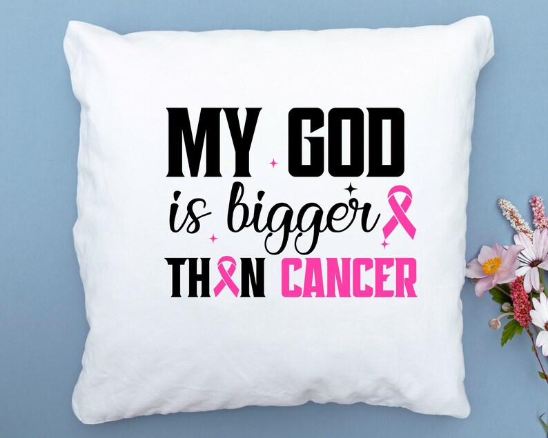 Puede incluir: Coj&iacute;n cuadrado blanco con el texto "MY GOD is bigger THAN CANCER" en negro y rosa. Un lazo rosa est&aacute; incluido en el dise&ntilde;o. El coj&iacute;n est&aacute; sobre una superficie azul claro.
