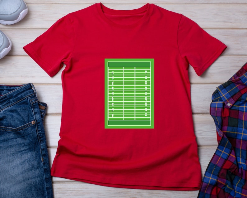May include: Red t-shirt with a green football field graphic on the front. The field has white lines and numbers.