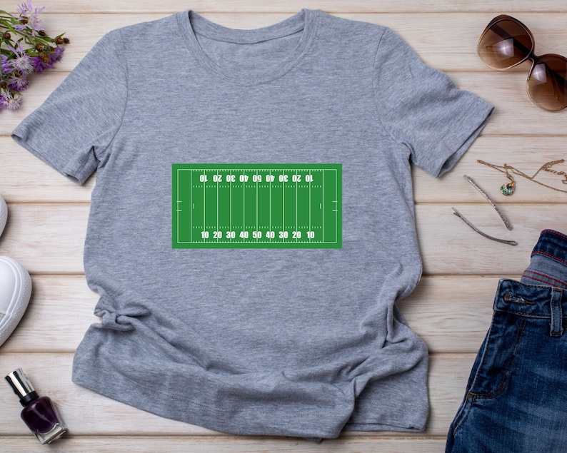 May include: A gray t-shirt with a green football field graphic printed on the front. The field has yard lines marked with numbers from 10 to 50.