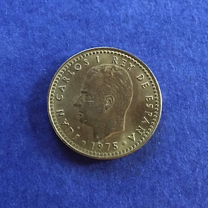 以下が含まれることがあります： 縁に「JUAN CARLOS I REY DE ESPANA」と「1975」の文字が刻まれた金色のコインです。