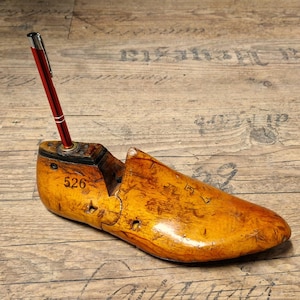 Op de afbeelding: Een houten schoenleest met een rode pen die in de bovenkant is gestoken. De leest is gemarkeerd met het nummer "526".