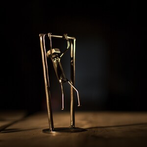 Peut inclure: Une sculpture en métal représentant une personne faisant un pull-up sur une barre en métal. La sculpture est faite de noix, de boulons et d'autres pièces de métal.