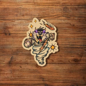 May include: A cartoon illustration of a purple and black cat with a lightning bolt and a tornado in the background. The cat is wearing a blue shirt and has a yellow tongue sticking out. The background is a light brown wood.