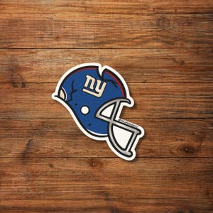 May include: A blue and white sticker of a football helmet with the letters "NY" on the side. The helmet has a white outline and a silver face mask. The sticker is on a wooden background.