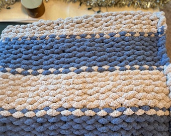 Könnte beinhalten: Eine blaue und beige gestrickte Wolldecke mit einem gestreiften Muster. Die Decke ist aus dickem Garn gefertigt und hat eine weiche, flauschige Textur.