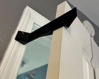 Può includere: Fermaporta in metallo nero a forma triangolare, montato su uno stipite di porta bianco.