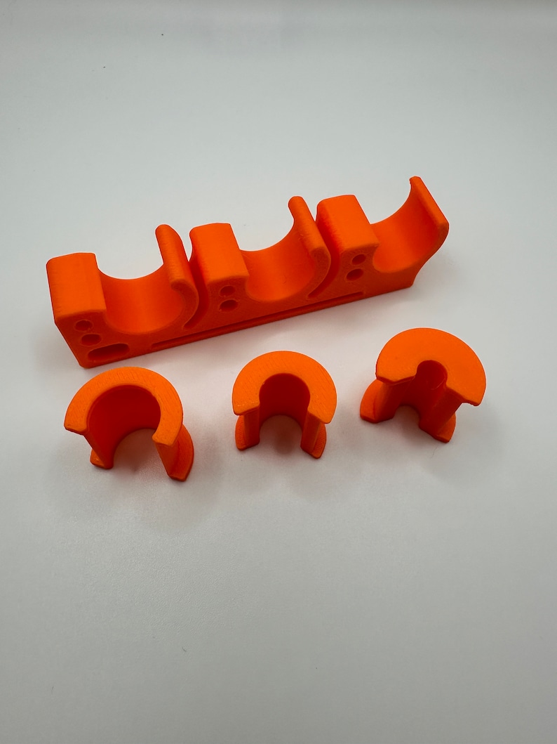 May include: Orange plastic pipe holder with three slots and three additional pieces. The holder is designed to hold pipes in place.