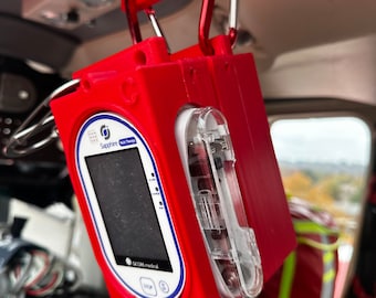 May include: A red medical device with a clear plastic window, labeled "Sapphire Auto-Inject", hanging from a red metal hook. The device has a small screen and buttons.