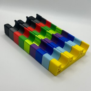 May include: A set of 10 colorful plastic pieces, each with a curved shape and a different color: black, red, green, lime green, purple, blue, light blue, yellow, and white.