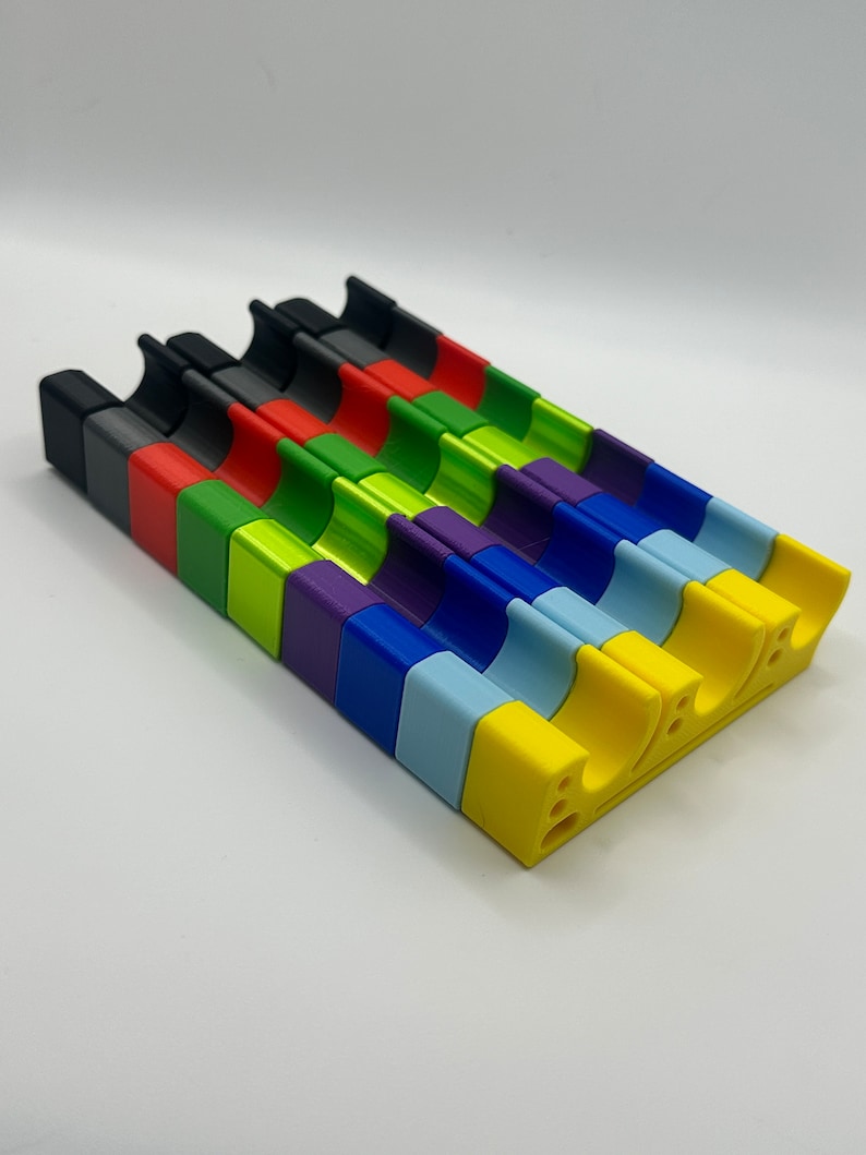 May include: A set of 10 colorful plastic pieces, each with a curved shape and a different color: black, red, green, lime green, purple, blue, light blue, yellow, and white.