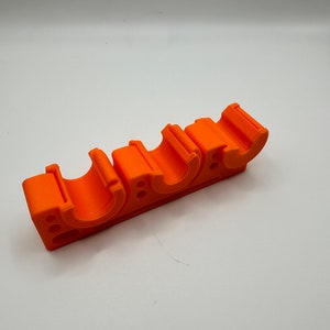 May include: Orange plastic pipe holder with four slots. The holder is designed to hold pipes in place.