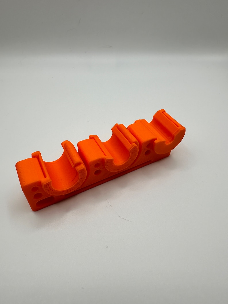 May include: Orange plastic pipe holder with four slots. The holder is designed to hold pipes in place.