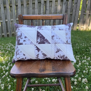May include: A white and purple patterned pillow with a quilted design. The pillow is sitting on a wooden chair.