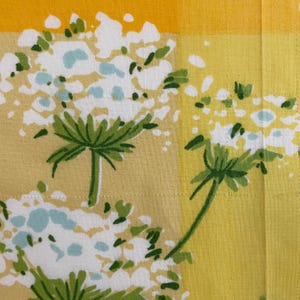 Puede incluir: Tela amarilla y blanca con un patr&oacute;n floral. Las flores son blancas con tallos y hojas verdes. La tela tiene un patr&oacute;n a cuadros.