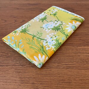 Puede incluir: Una tela amarilla con un patr&oacute;n de margaritas blancas y hojas verdes. La tela tiene el texto "Archer & Co. Daisy Plaid" impreso en ella.