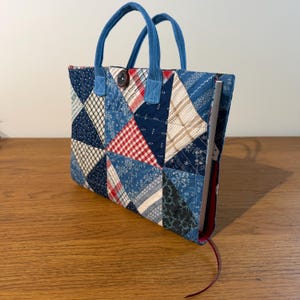 Könnte beinhalten: Eine Patchwork-Tragetasche mit blauen Griffen und einem Knopfverschluss. Die Tasche weist eine Vielzahl von Stoffen mit blauem, weißem und rotem Muster in einem geometrischen Design auf. Ein Buch ist im Inneren der Tasche sichtbar, mit einem roten Lesezeichen.