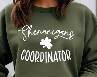 May include: A green sweatshirt with white text that reads "Shenanigans Coordinator" and a white four-leaf clover graphic.