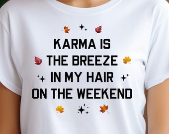 May include: A white short-sleeved t-shirt featuring the black text KARMA IS THE BREEZE IN MY HAIR ON THE WEEKEND. The design is accented with small black four-pointed star icons and colorful autumn leaf illustrations in red, orange, and yellow.