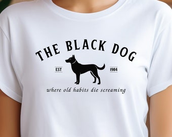 May include: White t-shirt featuring a black graphic of a dog and the text "THE BLACK DOG" above the dog, with "EST 1984" and the phrase "where old habits die screaming" below. The shirt is made of a soft material.