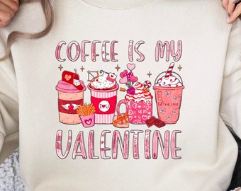 May include: A cream-colored sweatshirt with the text "Coffee is my Valentine" in pink lettering. The graphic features a row of four coffee drinks decorated with hearts and stars.