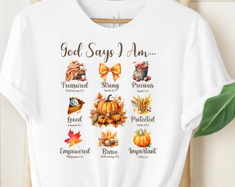 May include: A white short-sleeve t-shirt featuring a graphic with the text God Says I Am and various autumn-themed illustrations including pumpkins, a bow, a pie, and leaves, each paired with a descriptive word like Treasured, Strong, and Precious.