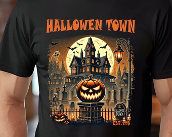 May include: A black short-sleeved t-shirt featuring a graphic print of a spooky mansion, a glowing jack-o'-lantern, and bats under a full moon. The text HALLOWEN TOWN and EST. 1998 are printed in orange. The design includes a cemetery and street lamp.