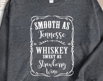 May include: Dark gray sweatshirt with a white rectangular graphic. The graphic reads "Smooth as Tennessee Whiskey, Sweet as Strawberry Wine" in a decorative font. The sweatshirt is a crew neck style.