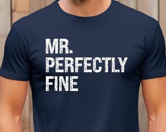 May include: Navy blue t-shirt with the text "MR. PERFECTLY FINE" in white, distressed lettering. The shirt is a classic crew neck style and is made of a soft material. The model is wearing blue jeans.