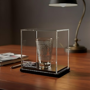 May include: A clear crystal shot glass with an etched Greek key and floral design, displayed in a clear acrylic case. The text on the case reads "From Dad's Cabinet Crystal Shot Glass Collected 1987 A Toast Remembered."