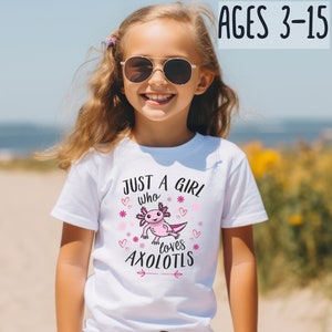 Könnte beinhalten: Ein weißes T-Shirt mit dem Text "JUST A GIRL who loves AXOLOTLS" und einer rosa Axolotl-Grafik. Das T-Shirt wird von einem jungen Mädchen mit Sonnenbrille getragen. Der Text "AGES 3-15" ist ebenfalls sichtbar.