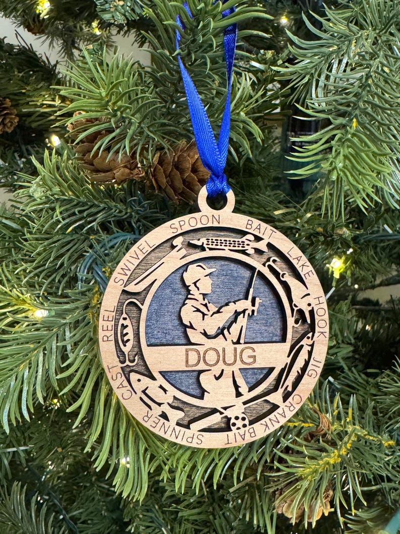 May include: Wooden Christmas ornament featuring a silhouette of a person fishing with the words "BAIT" and "SPOON" on the top and "CRANK BAIT" and "JIG HOOK" on the bottom. The ornament is personalized with the name "DOUG".