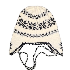 May include: White knitted hat with a black snowflake pattern and a black and white striped tie.