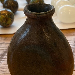 May include: A dark brown ceramic vase with a rounded body and a slightly flared opening. The vase has a textured surface and a subtle sheen.
