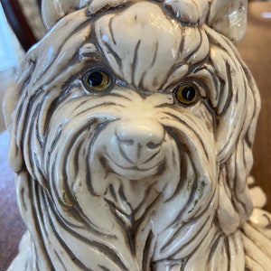 Peut inclure: Une sculpture en céramique blanche représentant un Yorkshire Terrier avec des yeux bruns. La sculpture est détaillée avec une fourrure texturée et une expression réaliste.