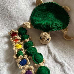 May include: A crocheted green turtle with a rainbow of smaller crocheted turtles lined up below it.