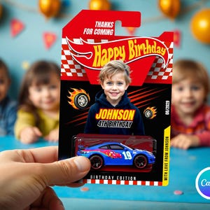 May include: A blue toy car with the number 19 is displayed on a birthday card. The card features a child's photo, the text "Happy Birthday," and "Johnson 4th Birthday." The card is held in a person's hand.