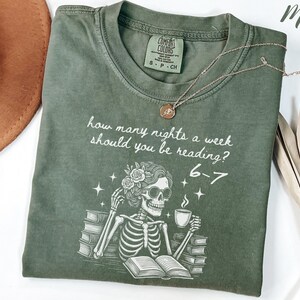 May include: Moss green Comfort Colors t-shirt with a skeleton graphic. The graphic includes the text "how many nights a week should you be reading? 6-7". The skeleton is holding a cup of coffee and wearing sunglasses.