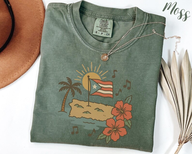 Op de afbeelding: Een mosgroen t-shirt met een afbeelding van de Puerto Ricaanse vlag, een palmboom en hibiscusbloemen. Het shirt heeft een ronde hals en korte mouwen. Het merklabel "Comfort Colors" is zichtbaar.