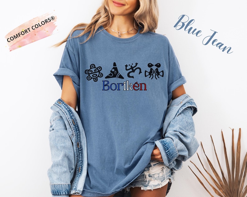 May include: A blue jean coloured t-shirt featuring the word "Borik&eacute;n" in blue and red, with black graphic designs above it. The shirt has short sleeves and a relaxed fit. The words "Comfort Colors" are in a pink banner.