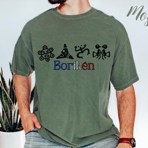 May include: A moss green t-shirt with black graphic designs and the word "Borik&eacute;n" in blue and red. The shirt has a relaxed fit and short sleeves. The word "Moss" is written in cursive in the upper right corner.
