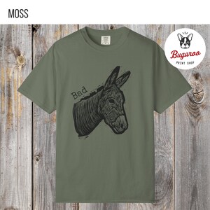 May include: Moss green t-shirt featuring a black illustration of a donkey's head with the word "Bad" above it. The shirt is from the Bugaroo Print Shop.