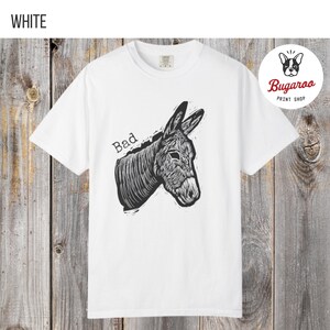 May include: White t-shirt featuring a black and white illustration of a donkey's head with the word "Bad" above it. The shirt has a crew neck and short sleeves. The Bugaroo Print Shop logo is in the upper right corner.
