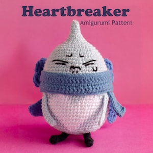 May include: A crocheted amigurumi figure with a grumpy face, wearing a blue scarf. The figure is primarily light blue and white, with black feet. The text "Heartbreaker Amigurumi Pattern" is at the top.